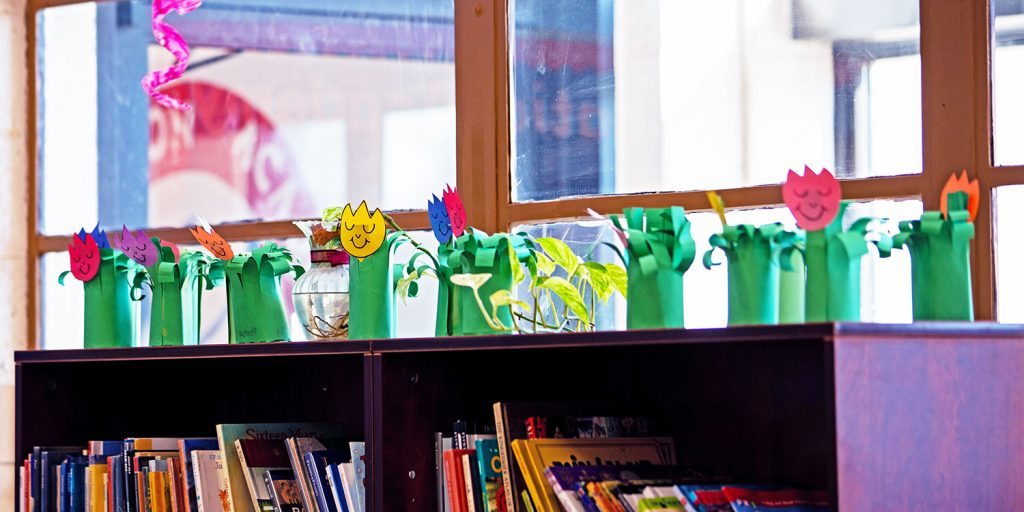 Flower art projects displayed on a bookshelf by a window.